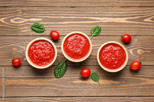 Bowls with tasty tomato sauce and fresh vegetables on wooden background