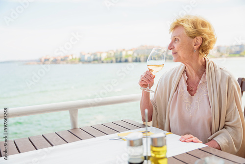 Mature attractive woman traveler sitting alone on the terrace of coffee shop and drinking rose wine. Active life of the elderly in retirement, active seniors