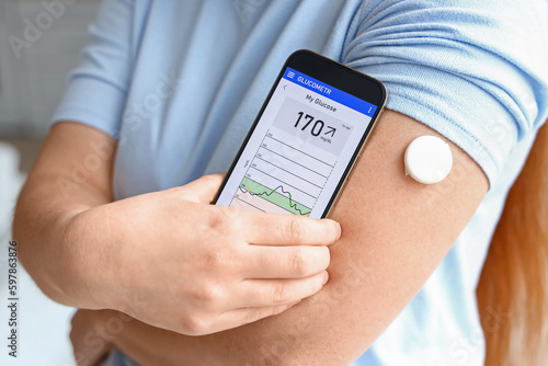Woman with glucose sensor using mobile phone for measuring of blood sugar level, closeup