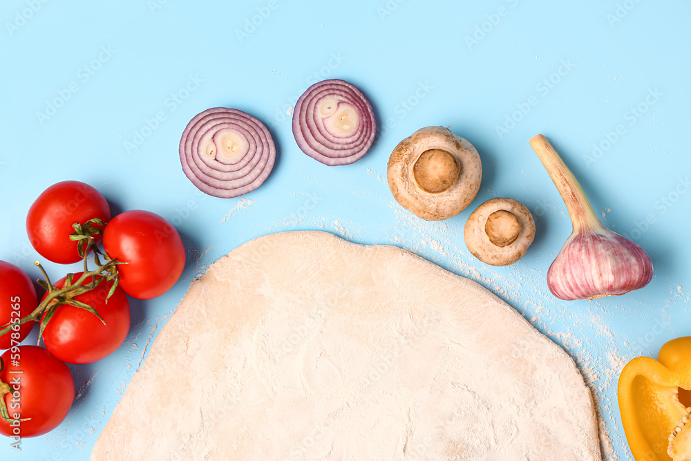 Fototapeta premium Fresh pizza dough with tomatoes, mushrooms, onion, garlic, and bell pepper on blue background, top view