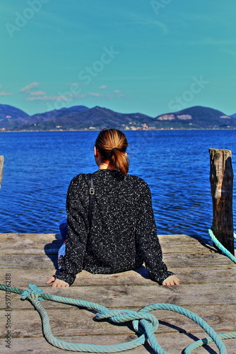Guardando il mare in solitudine. Giovane donna con la pelle chiara e i capelli castano chiaro, vestita con una giacca nera a pois bianchi, che guarda il mare che ha di fronte a Torre del Lago Puccini