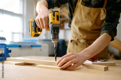 Carpenter working with drill leaning over table at carpentry workshop photo