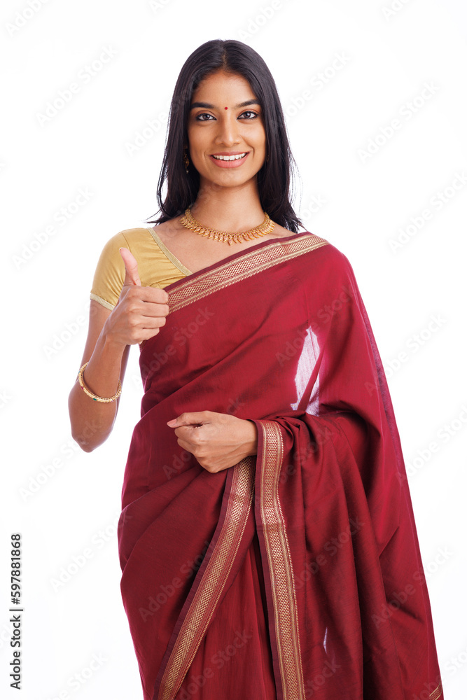 Indian woman smiling at the camera while showing thumbs up and wearing saree clothes in the studio shot.