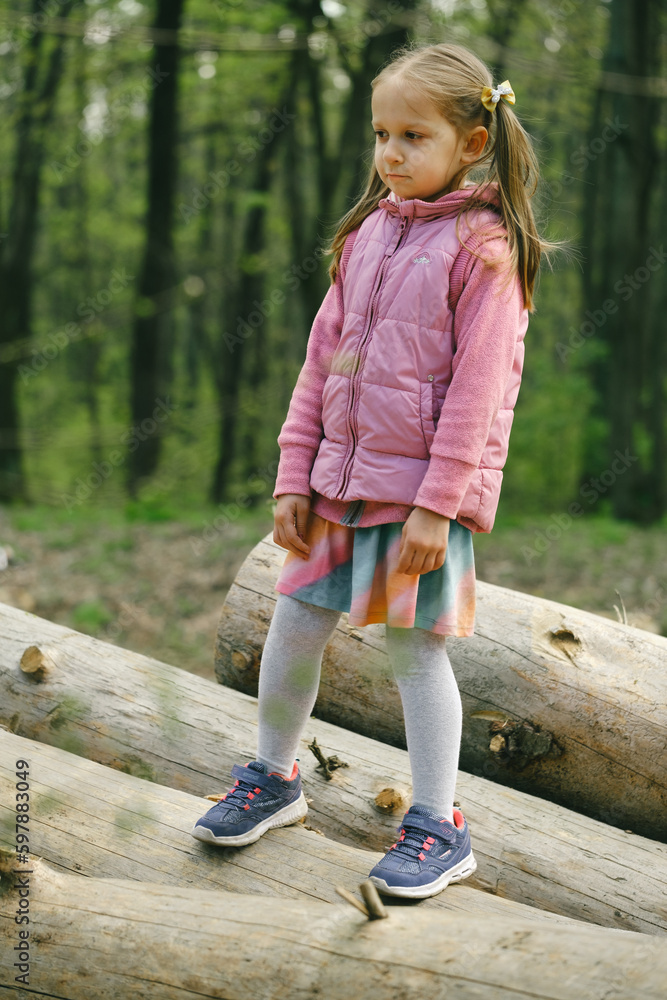 Fototapeta premium Child standing on big logs in the forest. Deforestation and human. Little girl inspects the site of deforestation