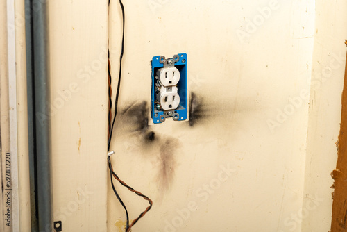 Electrical outlet with burn marks on wall from short circuit.
