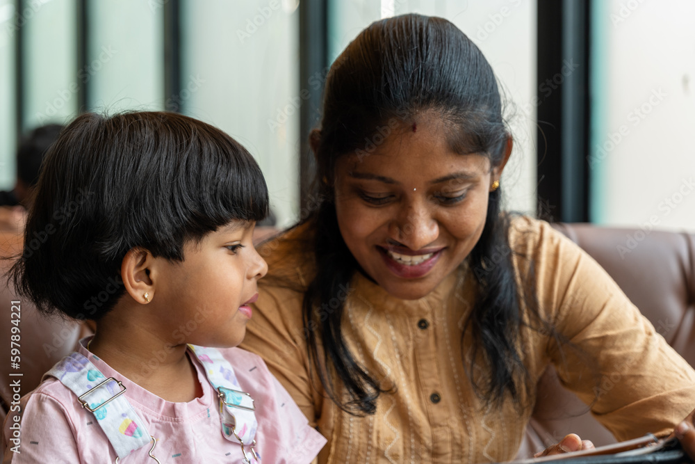 Mom and daughter checking food in restaurant menu card with smile both fully happy and check the dish Mom and daughter checking food in restaurant menu card with smile both fully happy and check the dish
