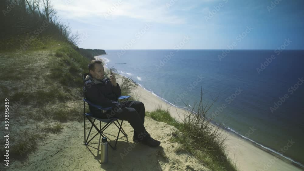 Man sitting in a chair drinking tea on a cliff by the sea. Man sitting in a chair drinking tea on a cliff by the sea.