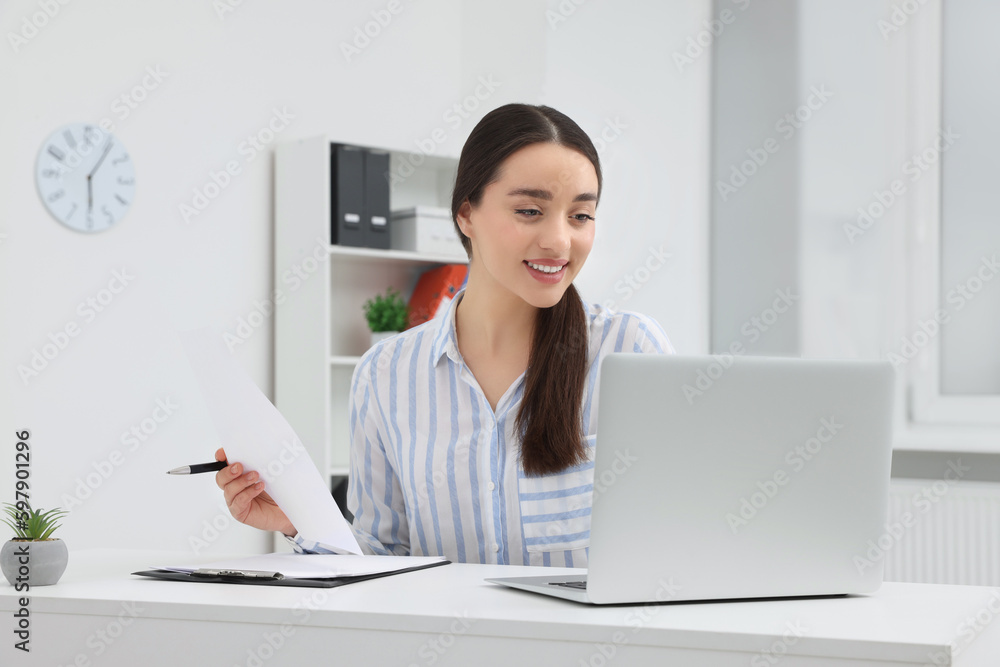 Young female intern working with laptop at table in office Young female intern working with laptop at table in office