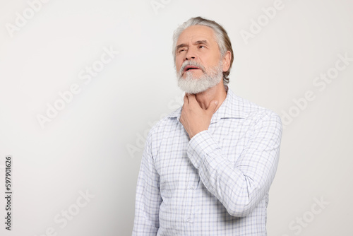 Senior man suffering from sore throat on white background, space for text. Cold symptoms