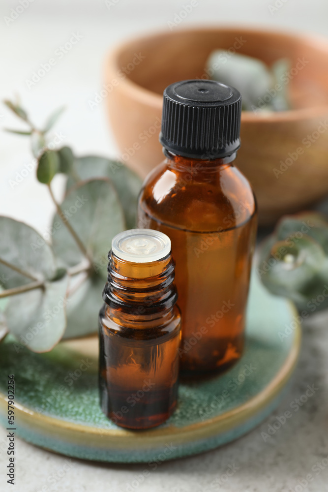 Bottles of eucalyptus essential oil and plant branches on light grey table Bottles of eucalyptus essential oil and plant branches on light grey table