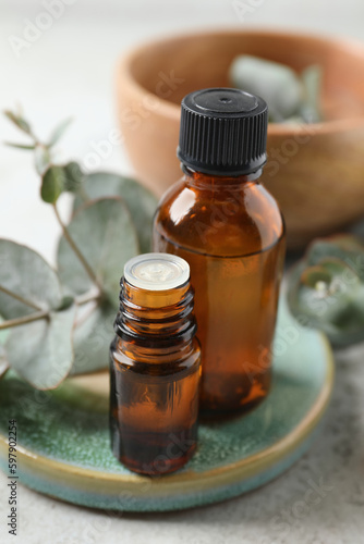 Bottles of eucalyptus essential oil and plant branches on light grey table