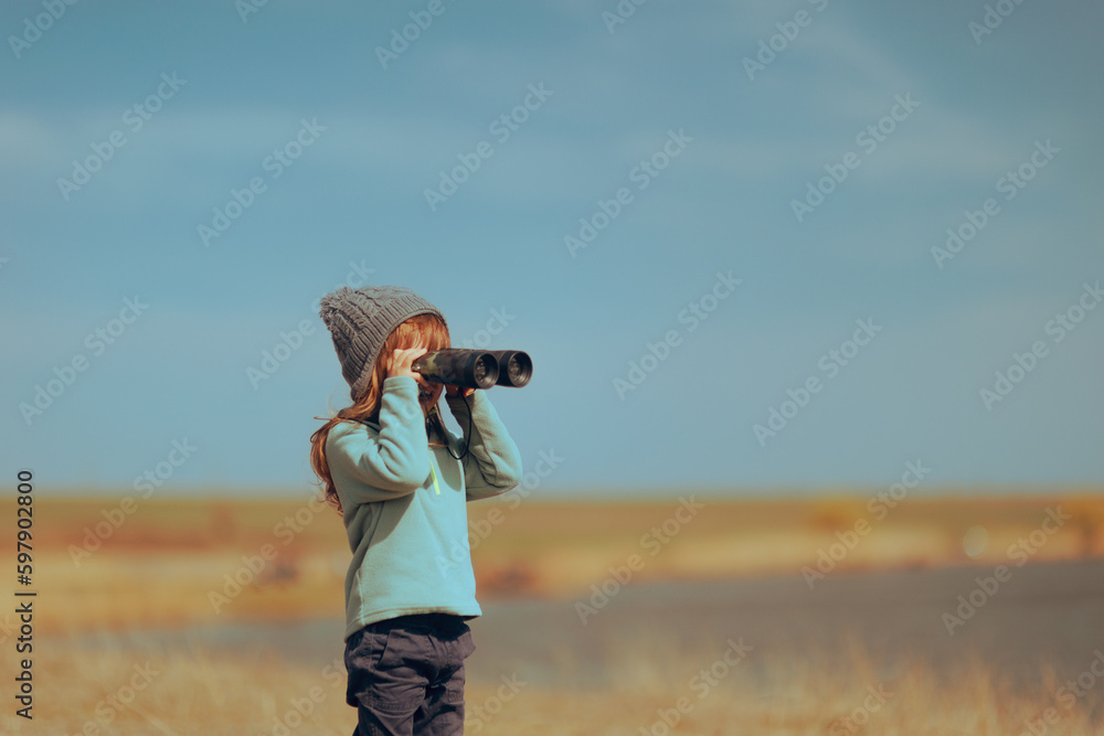Little Girl using a Binocular Checking Nature Outdoors. Curious child observing scenery using a pair of binoculars
