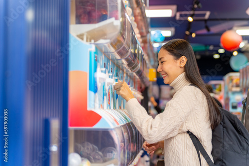 Happy Asian woman handle a doll from gashapon capsule toy vending machine while shopping at Tokyo city, Japan. Attractive girl enjoy and fun outdoor travel city street on autumn holiday vacation.