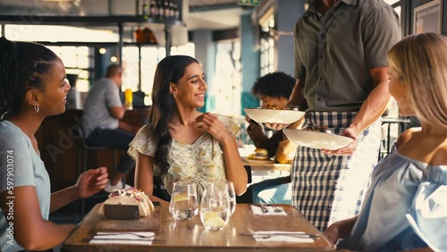 Group of multi-cultural female friends meeting in restaurant being served meal by waiter- shot in slow motion