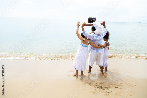 Black family having fun on the beach. mixed race family relaxing at the beach on summer holiday. Daughter in father arms or piggy back. photo