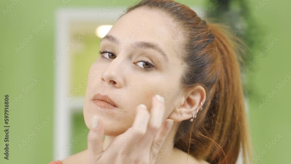 Young woman applying care to her facial skin.