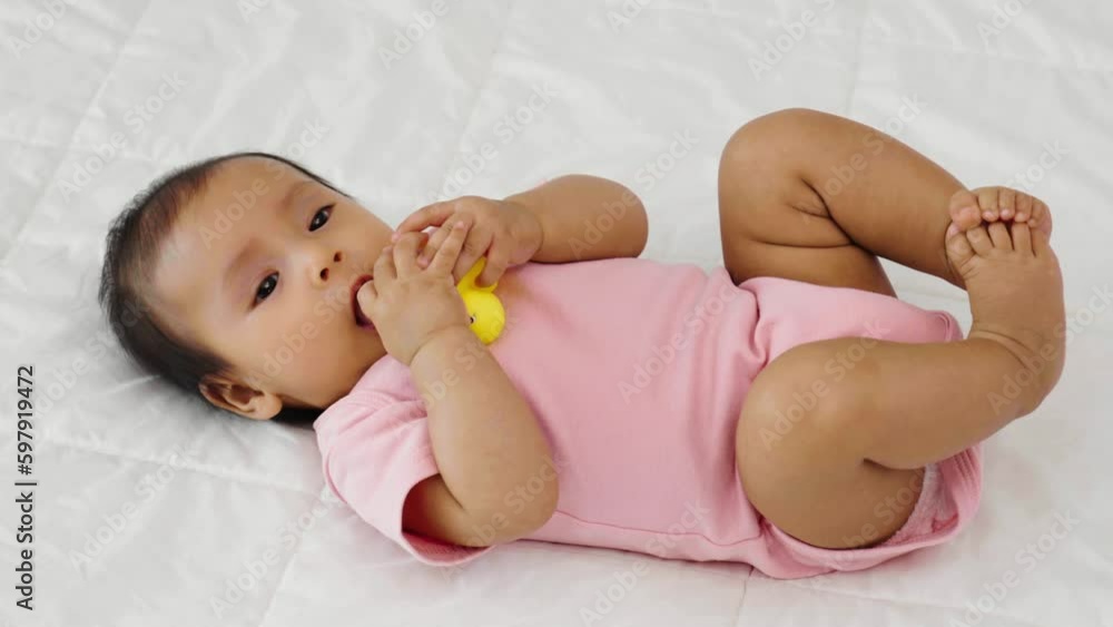 infant baby putting hands in mouth with sucking fingers and yellow rubber duck toy on a bed infant baby putting hands in mouth with sucking fingers and yellow rubber duck toy on a bed