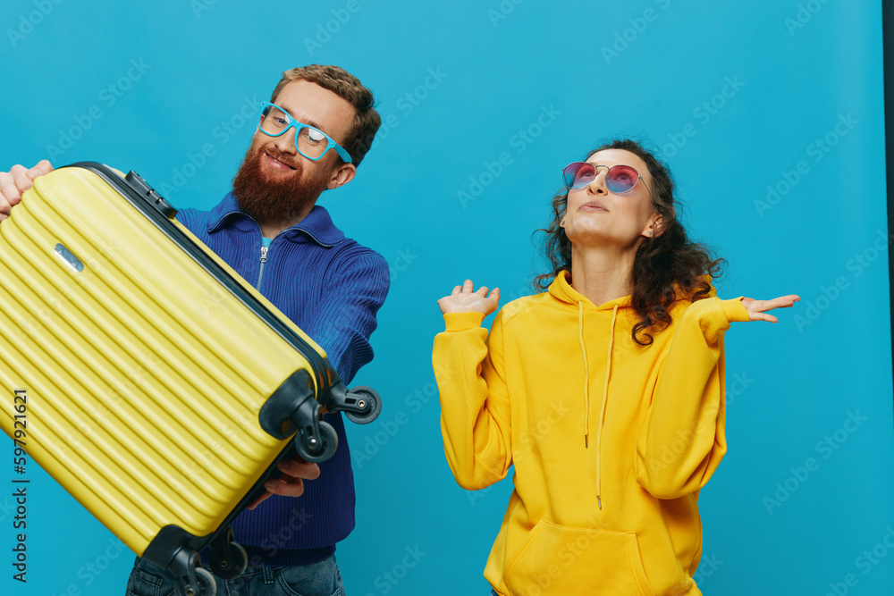 Woman and man smile sitting on suitcase with yellow suitcase smile, on blue background, packing for trip, family vacation trip.