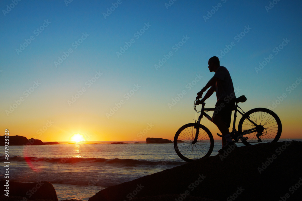 Man, beach and silhouette with mountain bike, sunset and mockup space by waves for summer cycling adventure. Cyclist, freedom and fitness with bicycle, training or journey by ocean in dusk sunshine