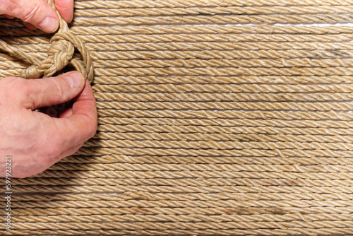 rough male fingers tying a knot from a rough rope, space for text