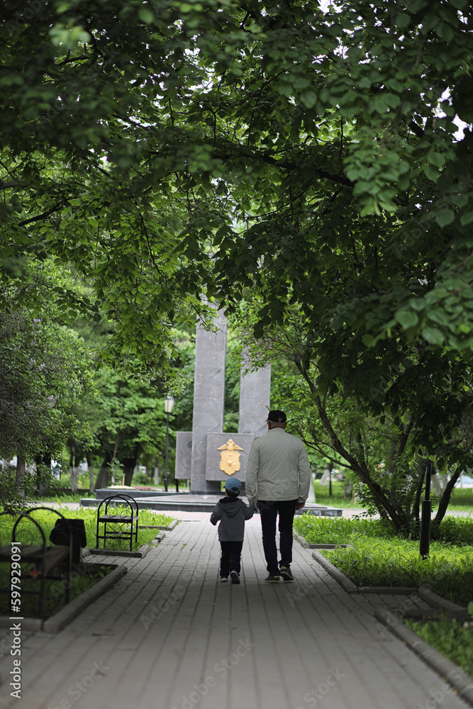 Grandpa is walking with her grandson in a spring park. Grandson and grandfather on a walk. Grandpa is talking to a little boy. Grandpa is walking with her grandson in a spring park. Grandson and grandfather on a walk. Grandpa is talking to a little boy.