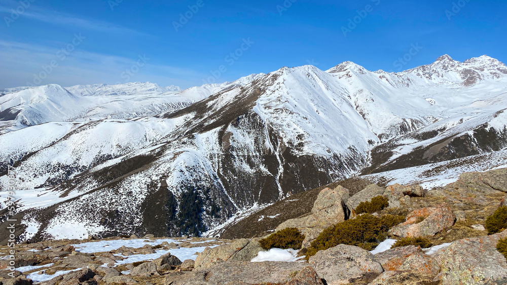 Snow-capped mountains, rocks and sparse vegetation. Beautiful view of the mountain landscape. Blue sky. The amazing nature of Kyrgyzstan.