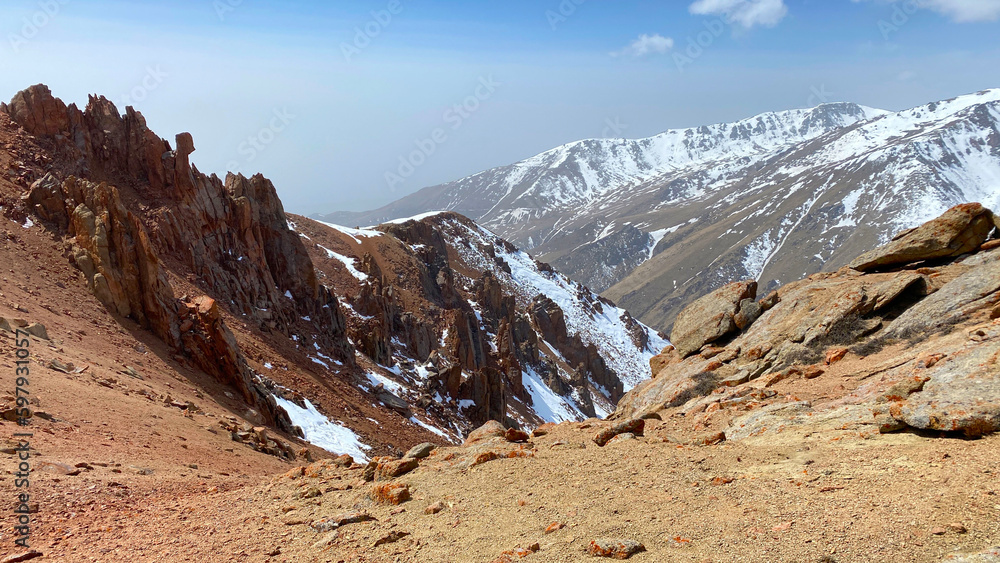 Amazing spring mountain landscape. Panorama of red rocky rocks and snow-capped mountains. Beautiful nature of Kyrgyzstan.