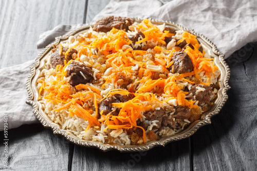 Traditional oriental pilaf with lamb topped with caramelized carrots, raisins and nuts close-up on a platter on a wooden table. horizontal photo