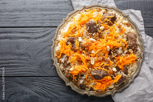 Traditional oriental pilaf with lamb topped with caramelized carrots, raisins and nuts close-up on a platter on a wooden table. horizontal top view from above photo