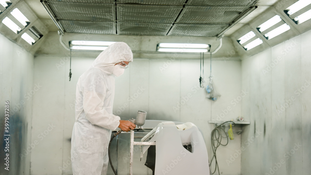 Fototapeta premium Caucasian car paint specialist in protective PPE suit Spraying air spray to paint a new car come out beautiful In the airless room of a car repair workshop Professionals work hard for