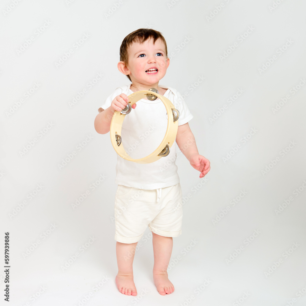 Happy baby play musical instruments on studio white background. Portrait of a smiling child and playing the tambourine. Kid about two years old (one year nine months) Happy baby play musical instruments on studio white background. Portrait of a smiling child and playing the tambourine. Kid about two years old (one year nine months)