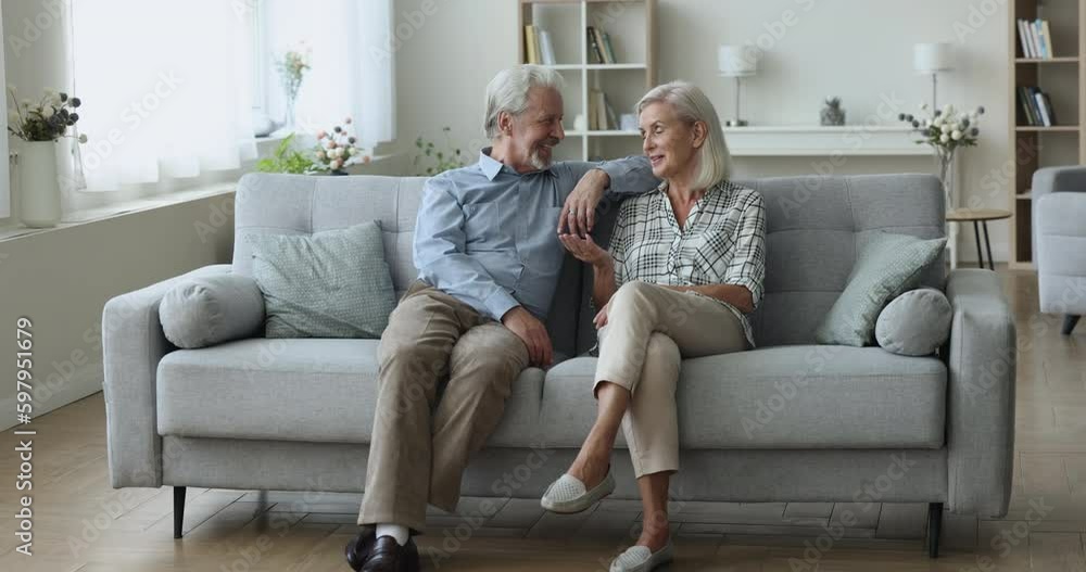 Retired couple sit, resting on sofa in living room having pleasant friendly conversation, enjoy harmonious relationship, discuss life situations, spend family pastime at home