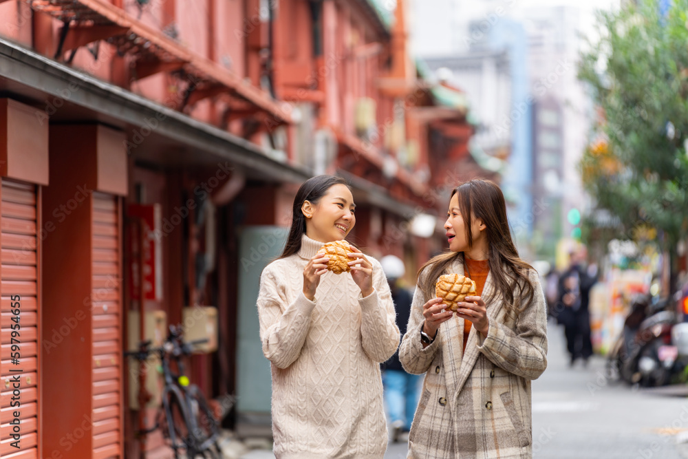 Obraz premium Happy Asian woman friends eating Japanese sweet bread together during travel at Asakusa, Tokyo, Japan. Attractive girl enjoy and fun urban outdoor lifestyle travel city street on holiday vacation.