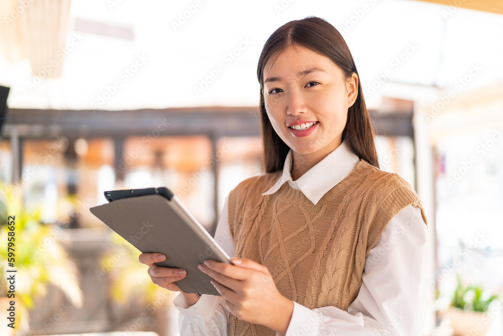 Young Chinese woman at outdoors holding a tablet with happy expression Young Chinese woman at outdoors holding a tablet with happy expression