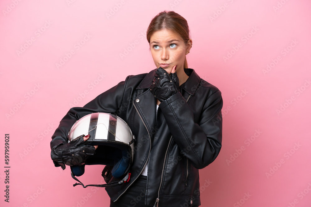 Young caucasian woman with a motorcycle helmet isolated on pink background having doubts Young caucasian woman with a motorcycle helmet isolated on pink background having doubts