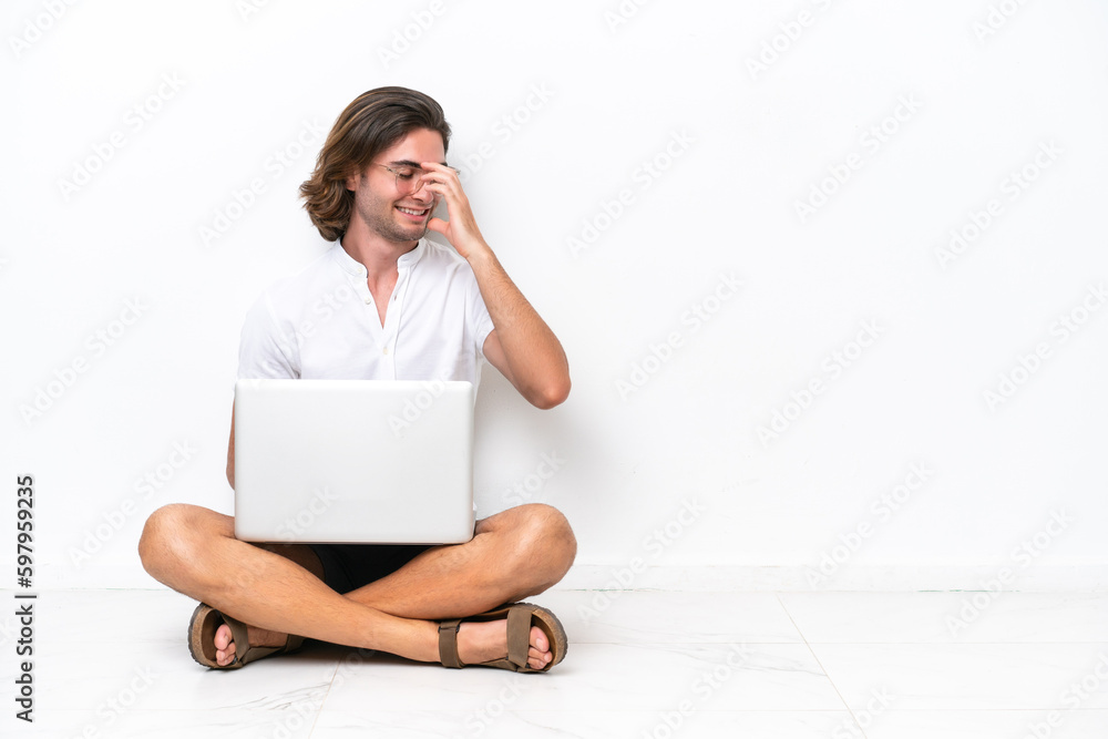 Young handsome man with a laptop sitting on the floor isolated on white background laughing Young handsome man with a laptop sitting on the floor isolated on white background laughing