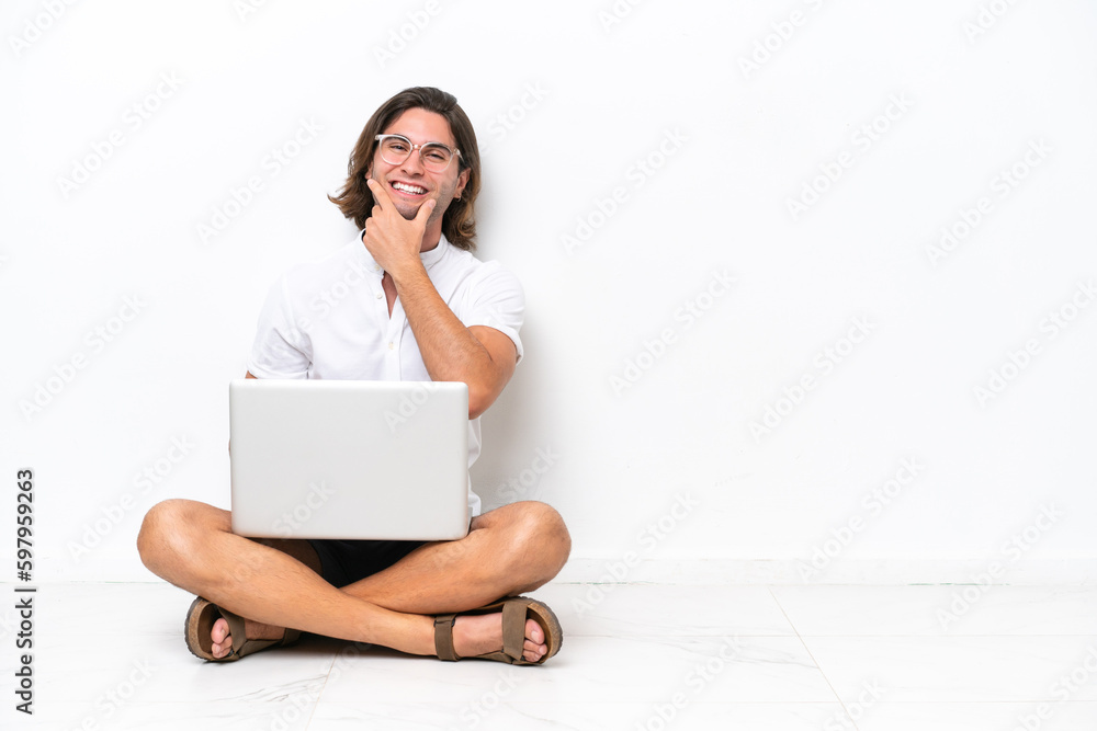 Young handsome man with a laptop sitting on the floor isolated on white background smiling Young handsome man with a laptop sitting on the floor isolated on white background smiling