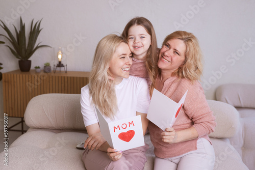 Happy Women's Day! The child's daughter congratulates her mother and grandmother, giving them flowers tulips. Grandmother, mother and girl smile and hug. Family holiday and unity.