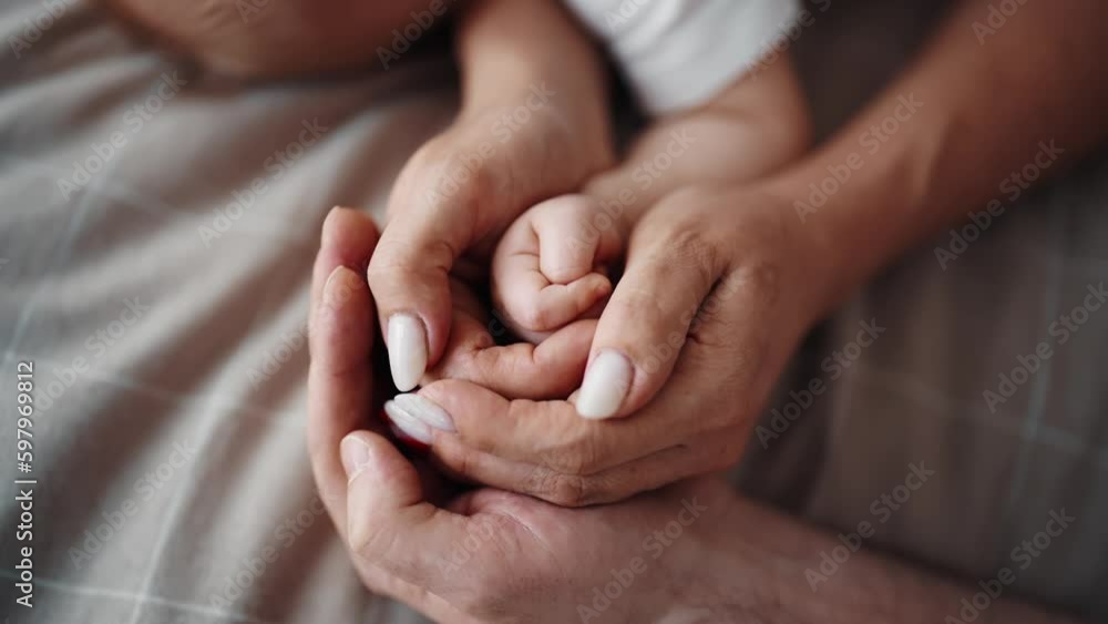 Close-up view of sleeping in bed baby's little hand in mom and dad's hands. Family love and babycare childcare, parenthood childhood concept. Mother, father and newborn child lying resting together. Close-up view of sleeping in bed baby's little hand in mom and dad's hands. Family love and babycare childcare, parenthood childhood concept. Mother, father and newborn child lying resting together.