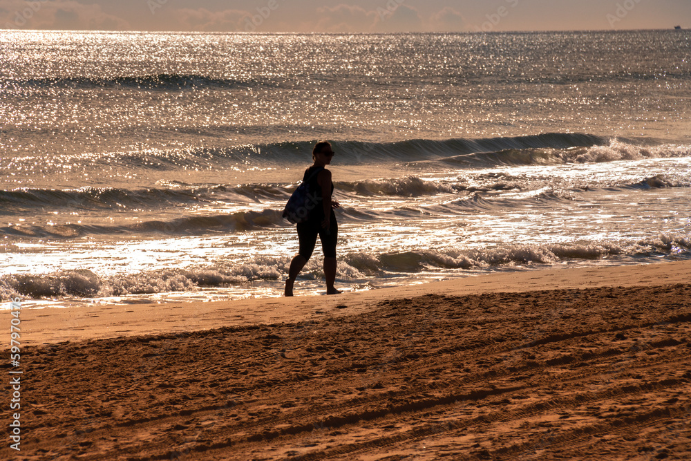 Φωτογραφία Silueta de mujer paseando por la orilla de la playa con un brillante amanecer