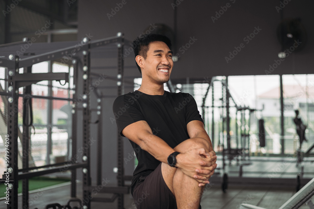 Strong asian man streching body before exercise at crossfit gym. Athlete male wearing sportswear warm-up before workout on grey gym background with weight and dumbbell equipment. Strong asian man streching body before exercise at crossfit gym. Athlete male wearing sportswear warm-up before workout on grey gym background with weight and dumbbell equipment.