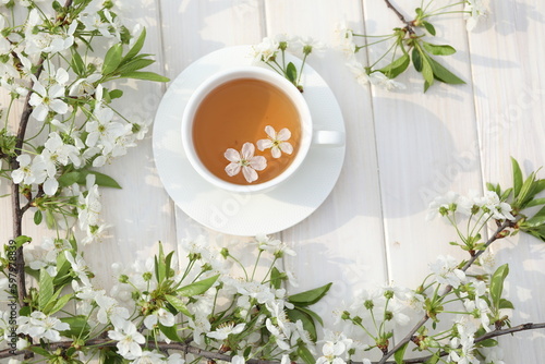 cup of tea with cherry blossom decoration on white wooden background.
