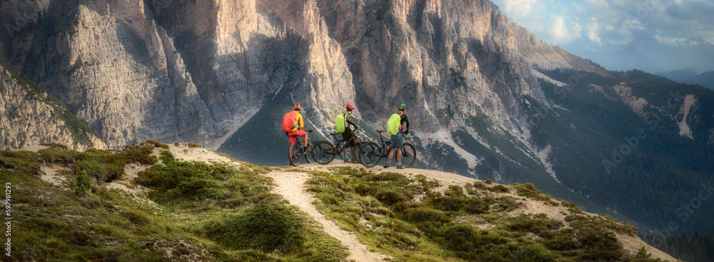 Friends mountain biking enthusiasts take a break, enjoy beautiful landscape, group of people on mountain bikes in Dolomites mountains landscape. Outdoor sport activity. Healthy lifestyle