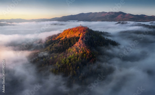 Drone view on the beautiful autumn mountains hills in low clouds at sunrise. Aerial view of Mountain peak with colorful forest in fog. Slovenia © kucherav