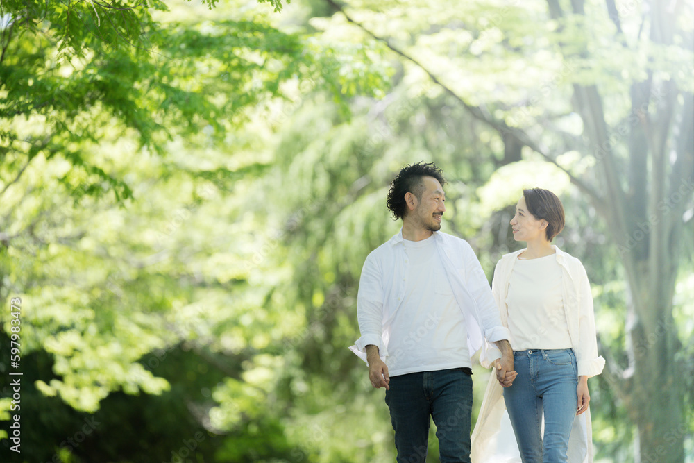 新緑の中夫婦で仲良く手をつないで歩く 見つめ合う 左にコピースペースあり 新緑の中夫婦で仲良く手をつないで歩く 見つめ合う 左にコピースペースあり
