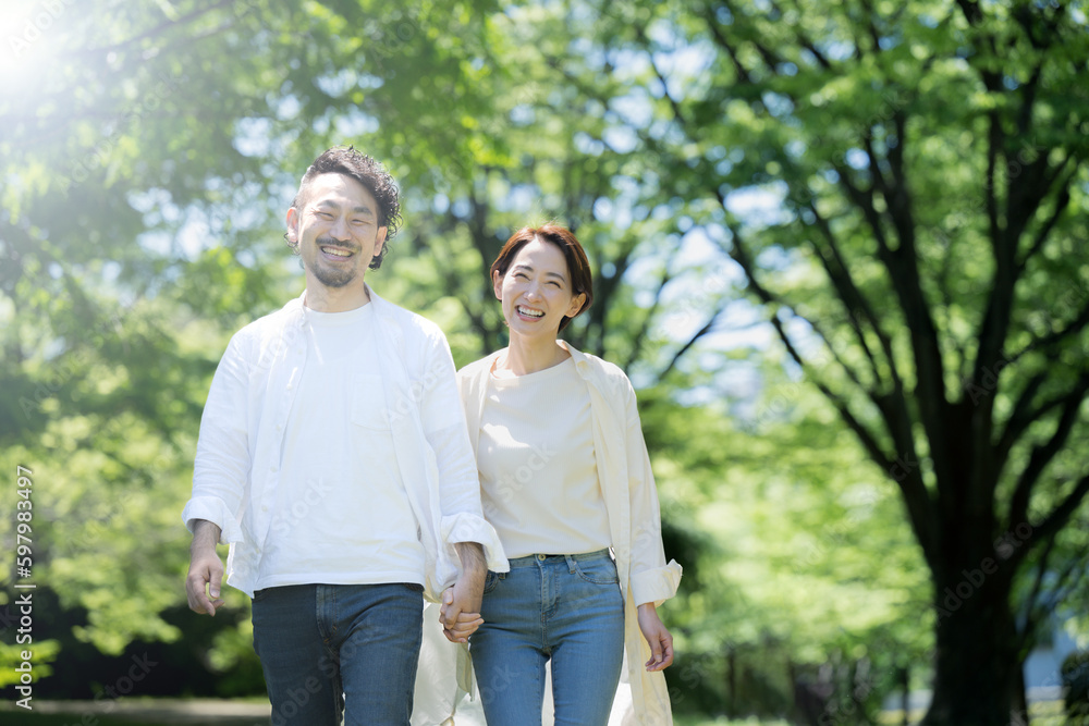 メインビジュアルにも!光の中新緑の中夫婦で仲良く手をつないで歩く カメラ目線 右にコピースペースあり メインビジュアルにも!光の中新緑の中夫婦で仲良く手をつないで歩く カメラ目線 右にコピースペースあり