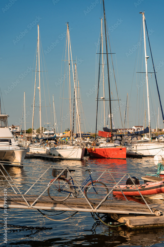 A blue bicycle is on a pontoon in the tourist port. In the background are boats and yachts docked in the port, in a hot summer afternoon
