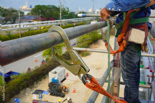 Hook of safety harness on scaffolding pipe during working at heights in construction site, Chemical plant.