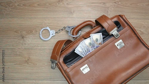 The handcuffs are fastened to a brown leather briefcase, from which money is visible. Camera movement from right to left.