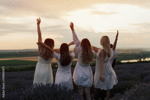 Silhouettes of five happy young girls with hands up standing and clinking wineglasses on beautiful sunset.